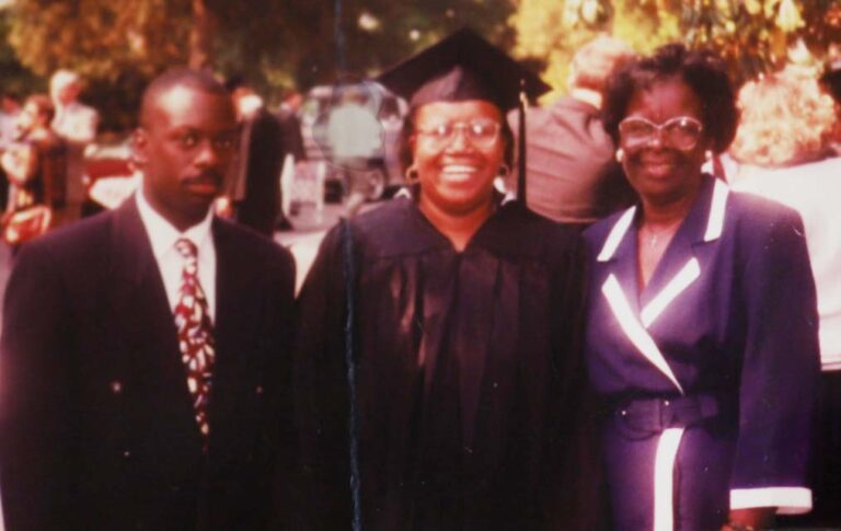 Three church members standing in front of a church wearing formal dress attire